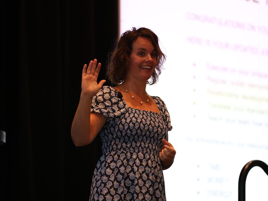A speaker smiles and raises her hand beside her slides during a workshop at a past retreat