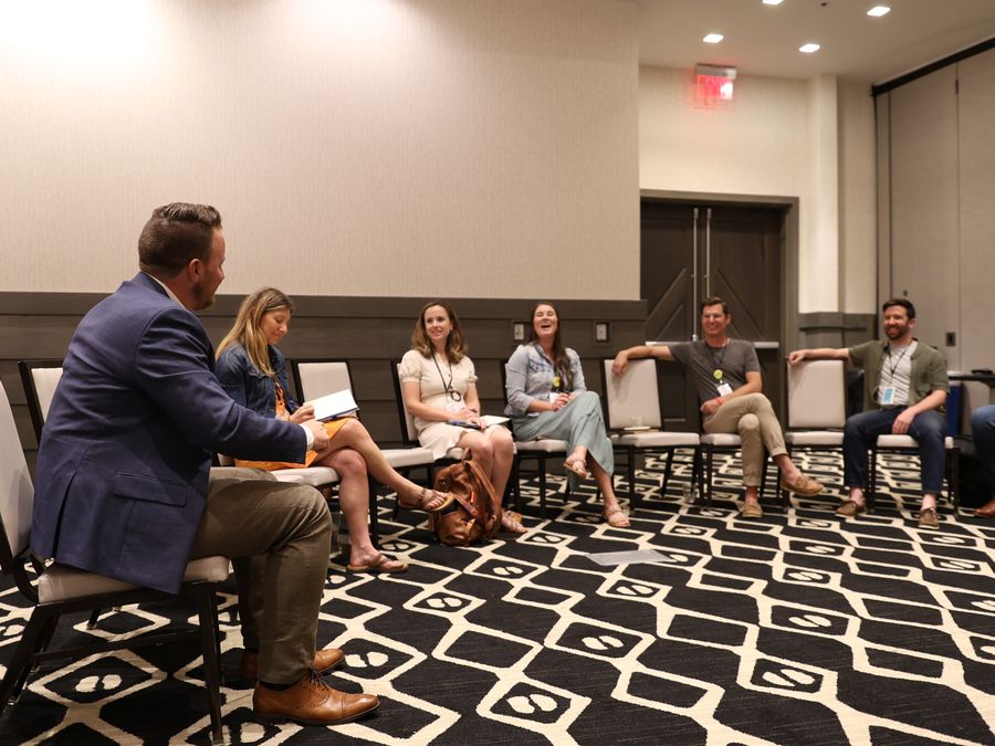 Agency owners sit in a circle of chairs, laughing as one of them talks through a problem