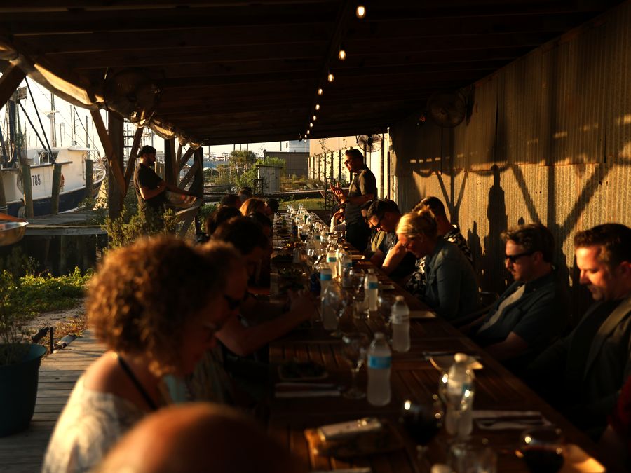 Guests share a long outdoor dinner table under string lights at golden hour